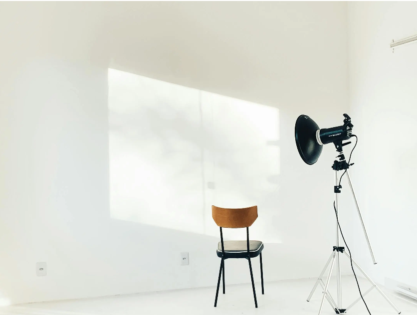 Minimalist studio setup with a wooden chair and a studio spotlight against a white wall